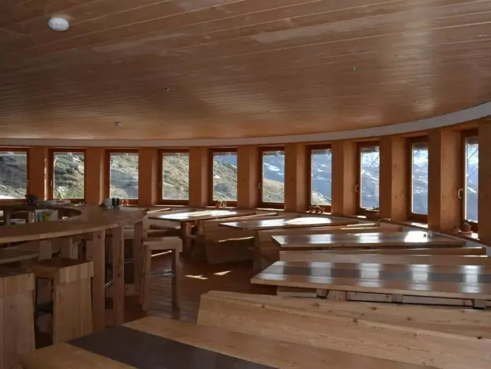 Salle a manger du refuge de l'Arpont en Savoie avec ces grandes tables en bois, magnifique bar et multiples fenetres offrant beaucoup de lumiere / Amenagement realise par ViolaDeco, Iana VIOLA