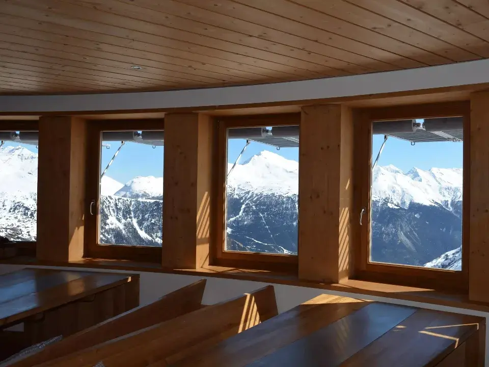 Salle a manger du refuge de l'Arpont en Savoie avec vue sur les tables et panorama des montagnes a travers les fenetres / Amenagement par ViolaDeco, Iana VIOLA 