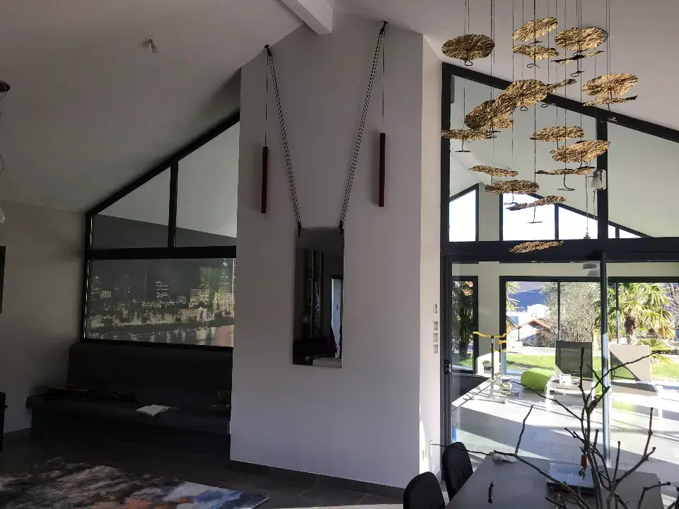 Salon design d'une villa avec grand miroir elegant avec chaines symetriques pour le maintenir, luminaires couleur doree, table, canape et magnifique veranda / decoration par ViolaDeco, Iana Viola